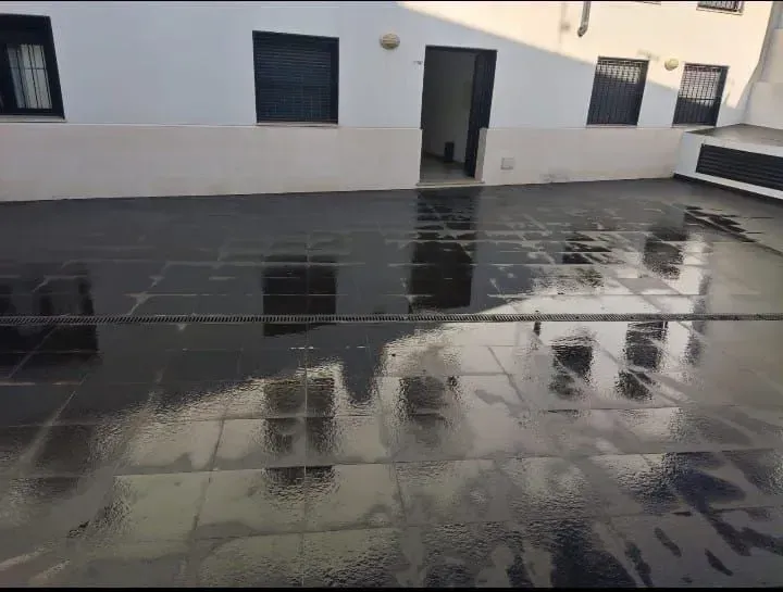 Un suelo de baldosas negras con un edificio blanco al fondo.