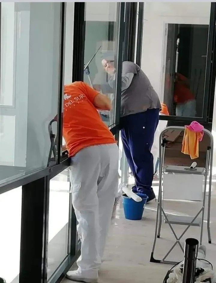 Un hombre con una camisa naranja está limpiando una ventana.