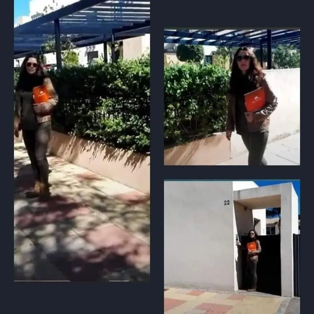 Una mujer camina por una acera sosteniendo un libro naranja.