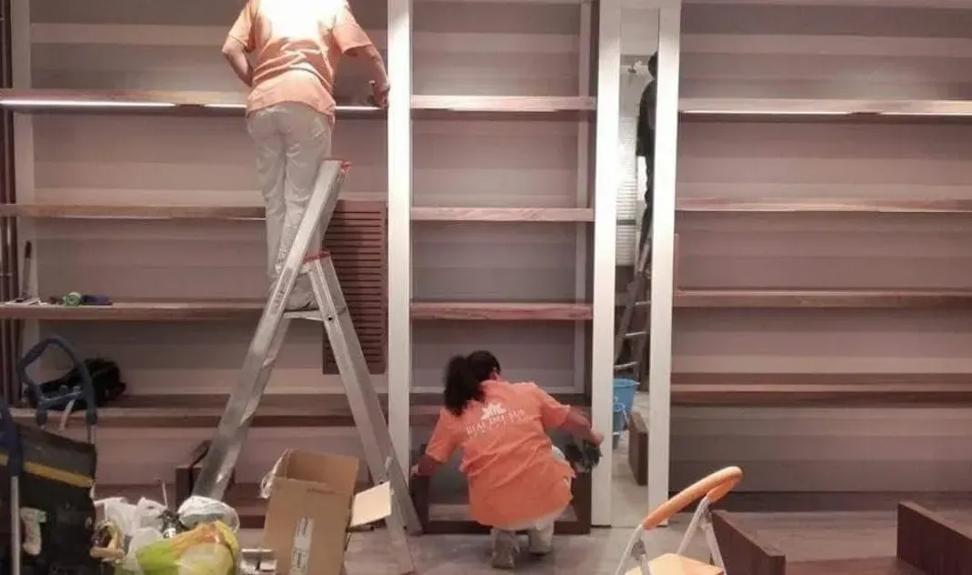 Una mujer está parada en una escalera frente a una pared de estantes.