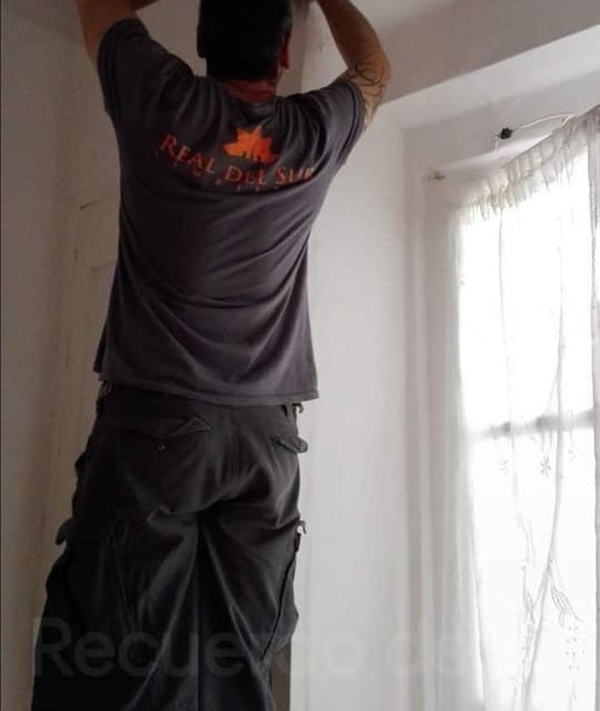 Un hombre que lleva una camiseta de bienes raíces está de pie en una escalera.