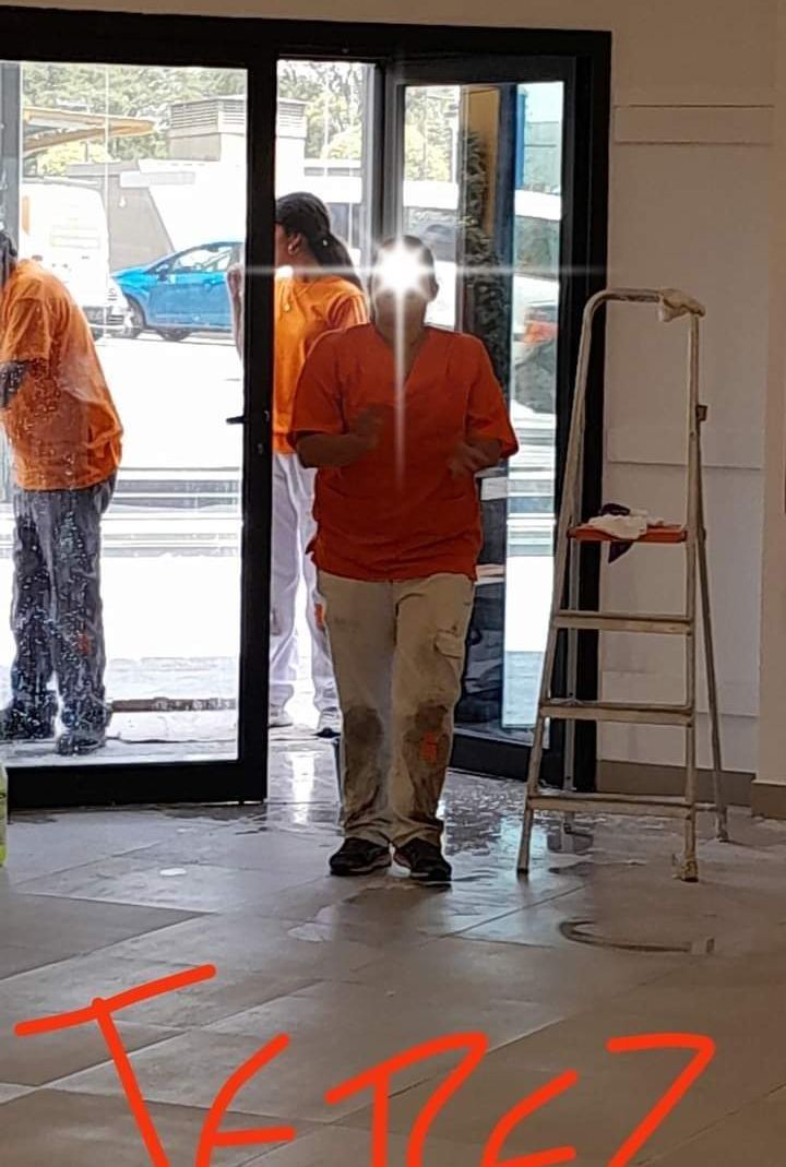 Un hombre con una camisa naranja está parado frente a una puerta de vidrio.