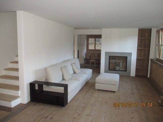 Ein Wohnzimmer mit Couch, Ottomane, Kamin und Treppe. Foto von der H. Kuhn Hoch- und Tiefbau AG