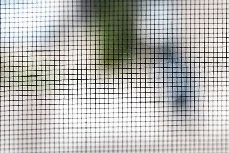 Primer plano de la mosquitera de una ventana, que oculta una vista borrosa de los árboles y el cielo.