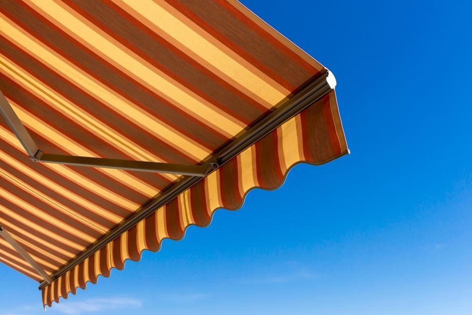 Toldo de rayas naranjas y crema contra un cielo azul brillante.