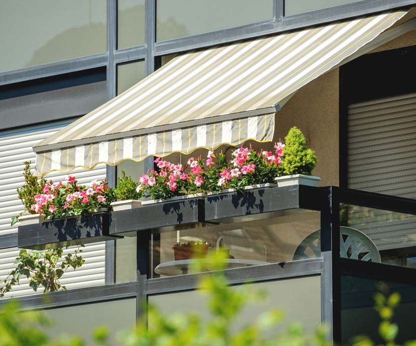 Un balcón con flores y un toldo de rayas.