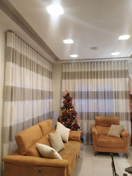 Sala de estar con sofá marrón, sillón, cortinas de rayas y árbol de Navidad.