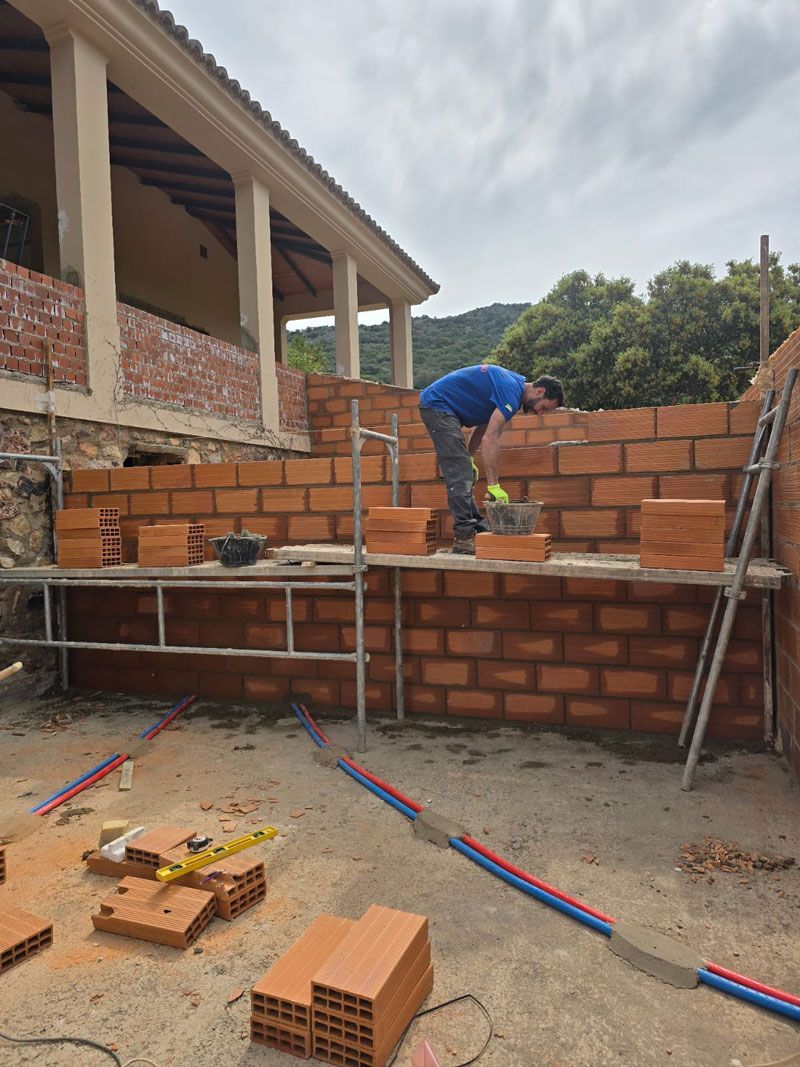 Un hombre está trabajando en una pared de ladrillos frente a un edificio.