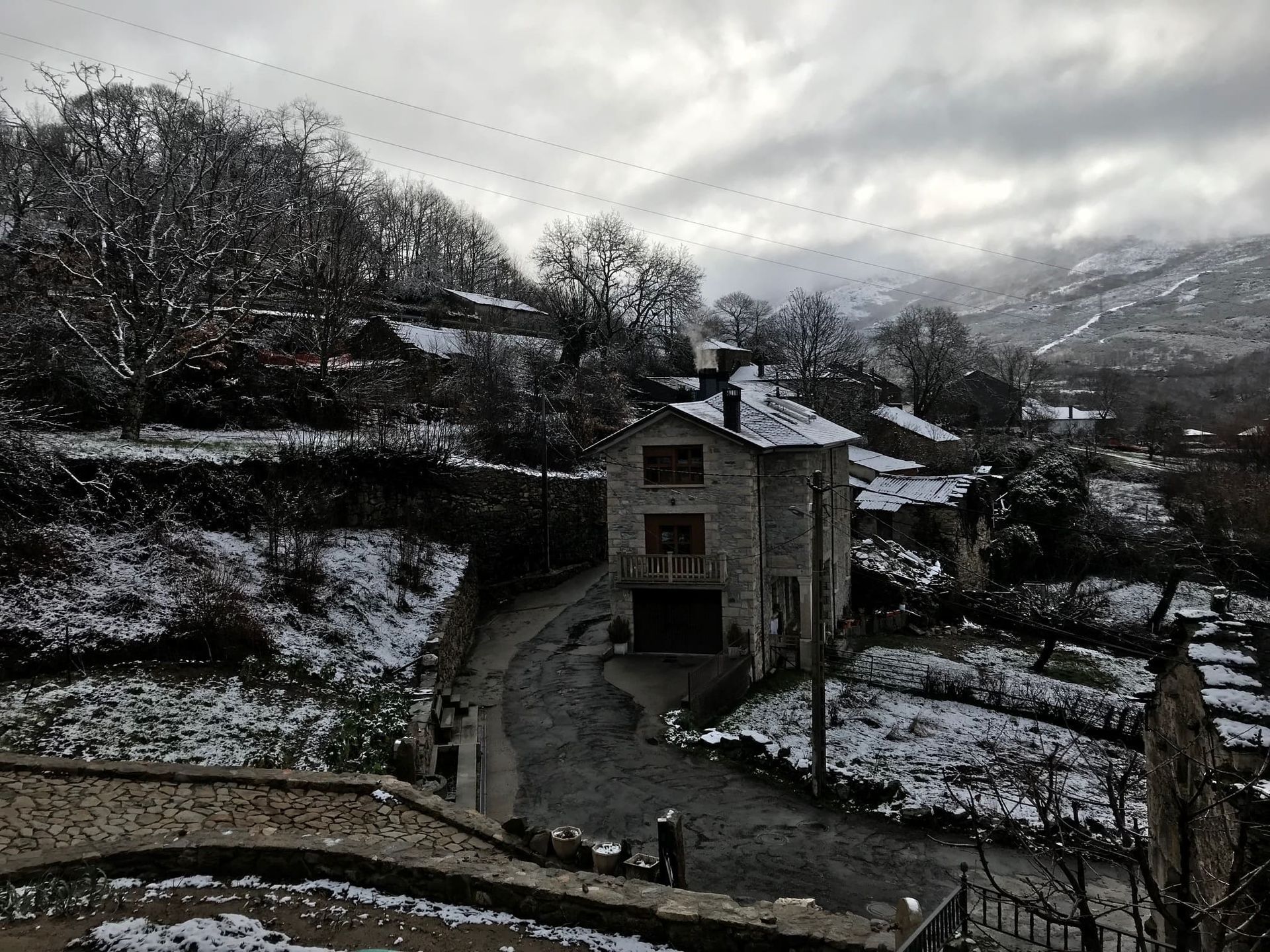 Escena de pueblo nevado con casas de piedra y camino que serpentea a través del paisaje bajo un cielo nublado.