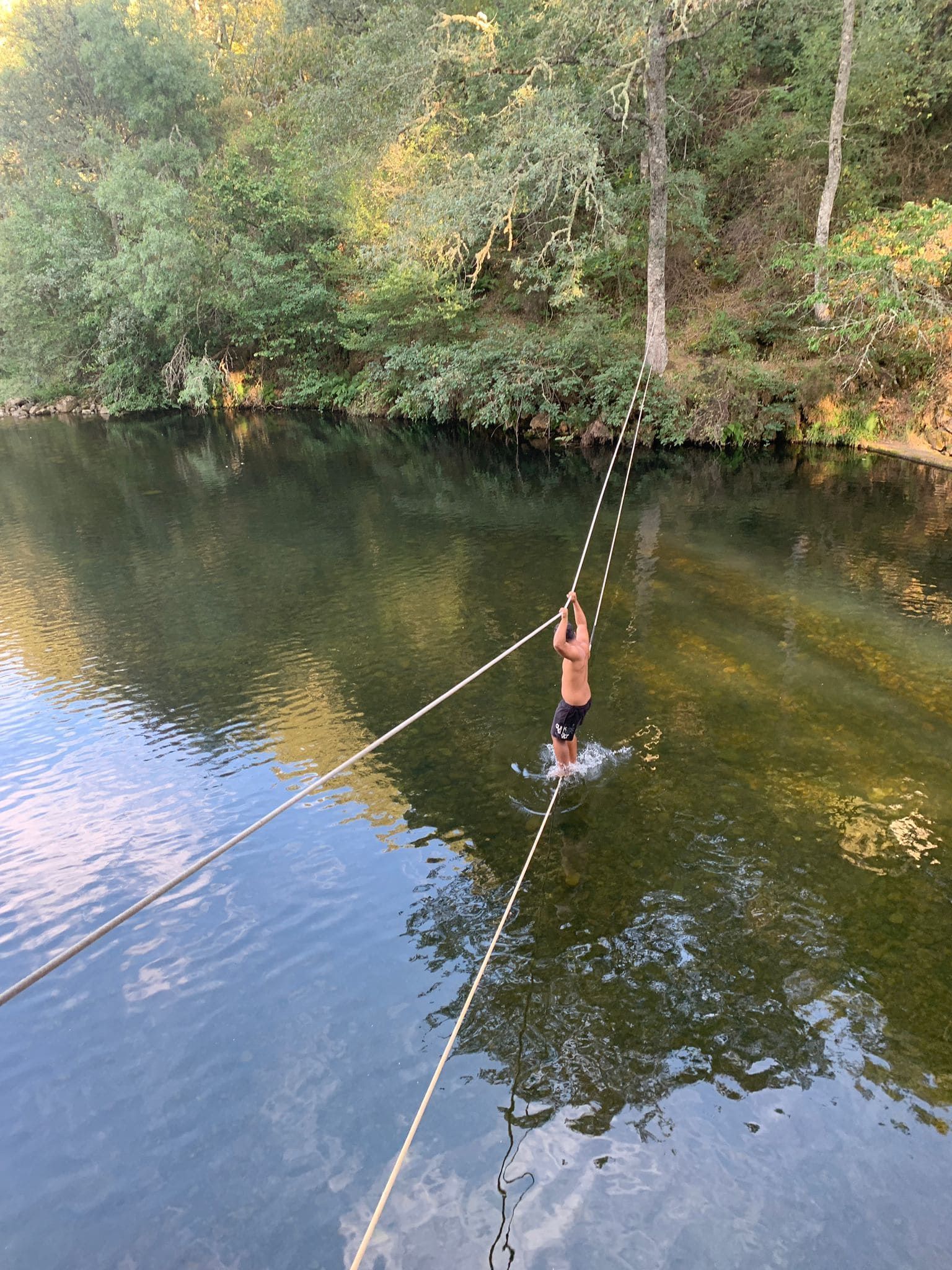 Persona balanceándose en una cuerda hacia el río.