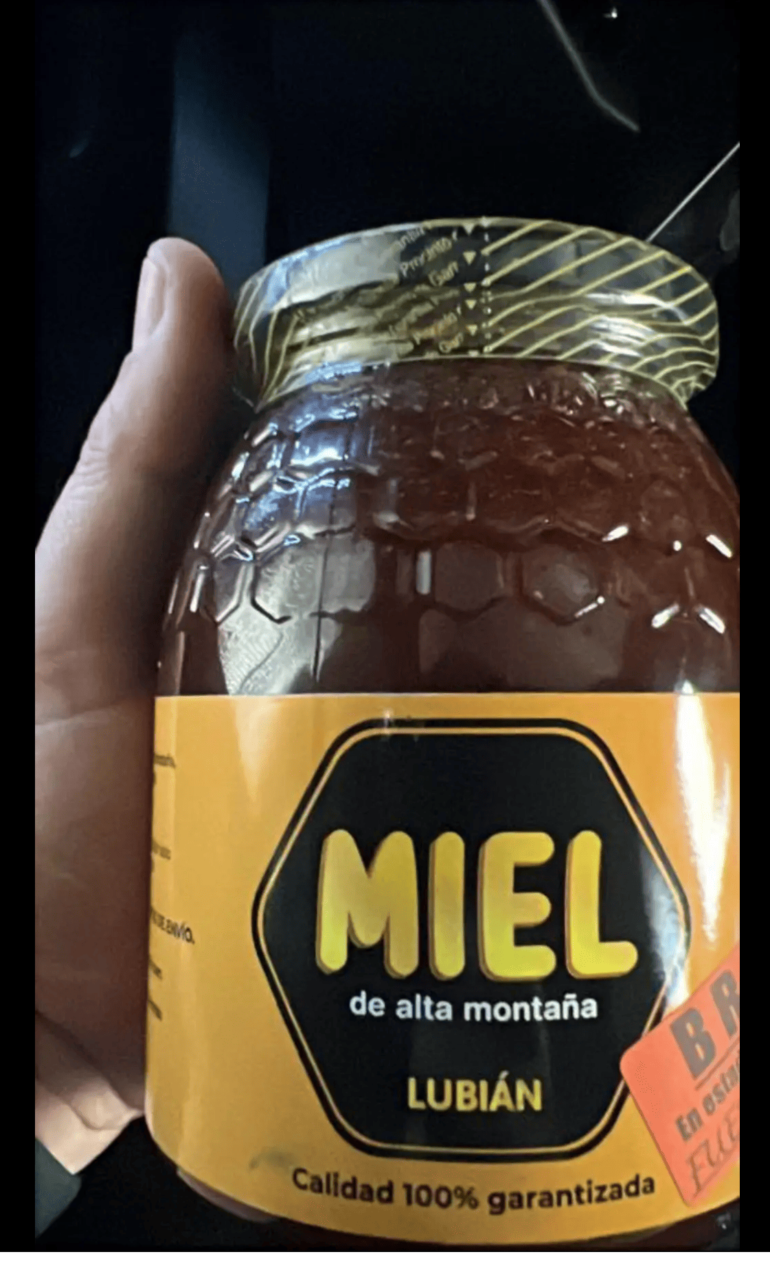 A hand holding a jar of honey labeled 