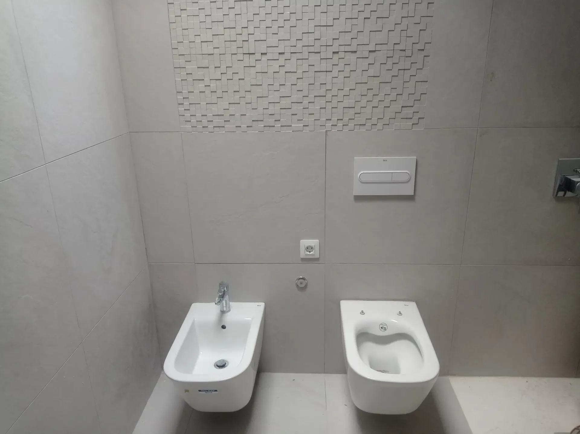 Baño gris moderno con bidé e inodoro, diseño de pared texturizada encima.
