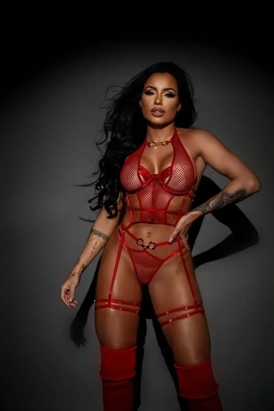 Mujer en lencería roja, posando sobre un fondo gris oscuro.