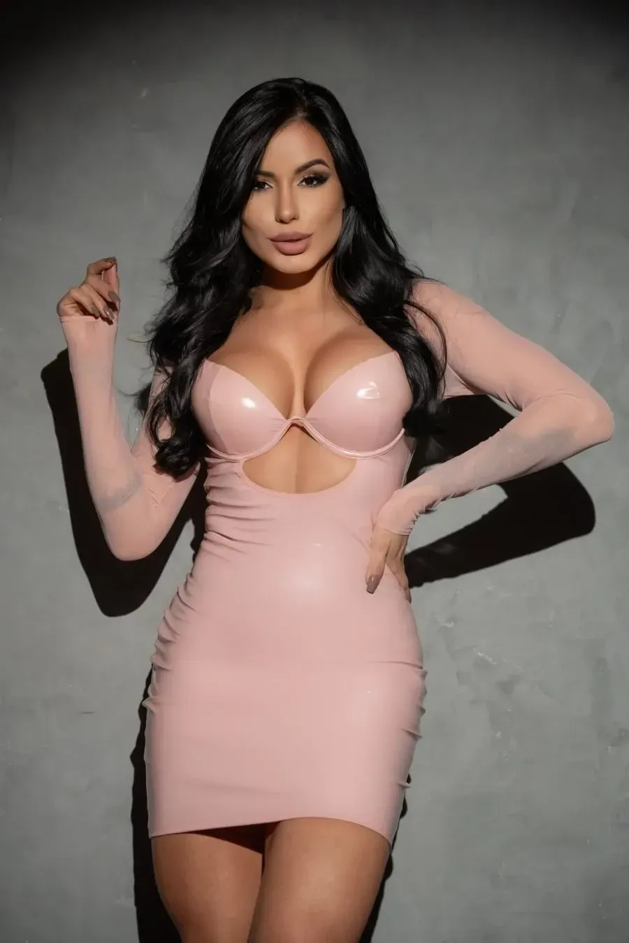 Mujer con vestido rosa ajustado con mangas largas, manos en las caderas, mirando a la cámara.