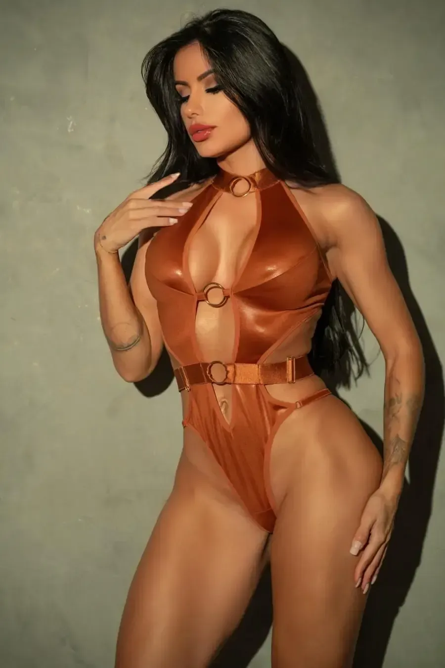 Mujer con traje de baño color bronce, posando. Detalles de aros, piernas de corte alto y top halter.