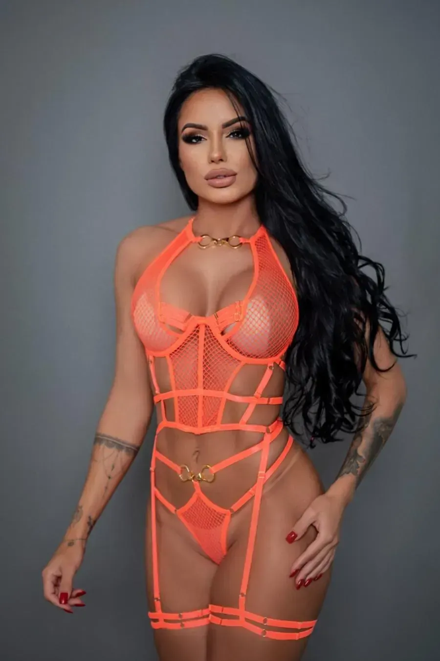 Mujer en lencería de color naranja neón con cabello largo y negro, posando frente a un fondo gris.