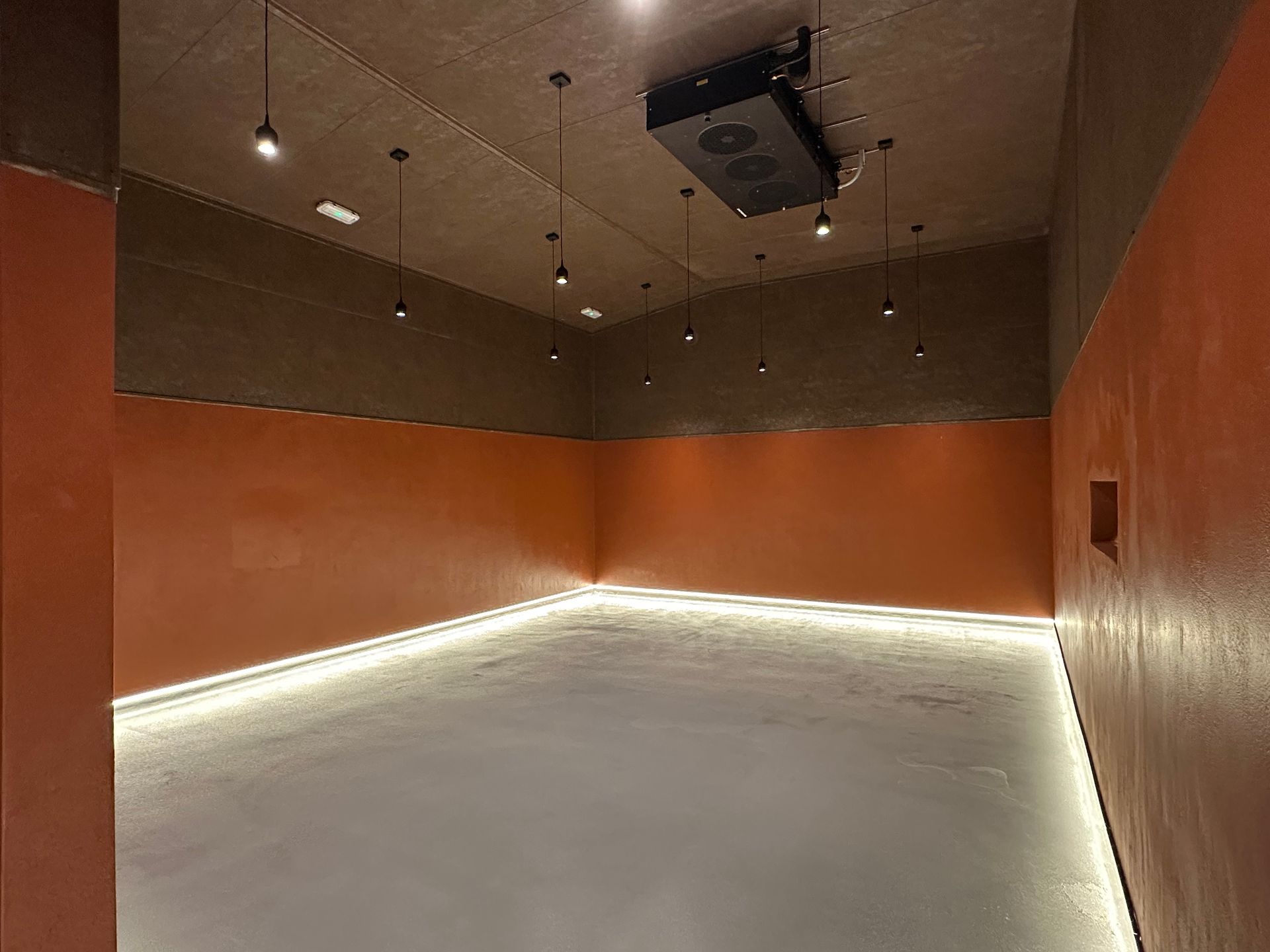 Habitación vacía con paredes naranjas, suelo blanco y luces en el techo.