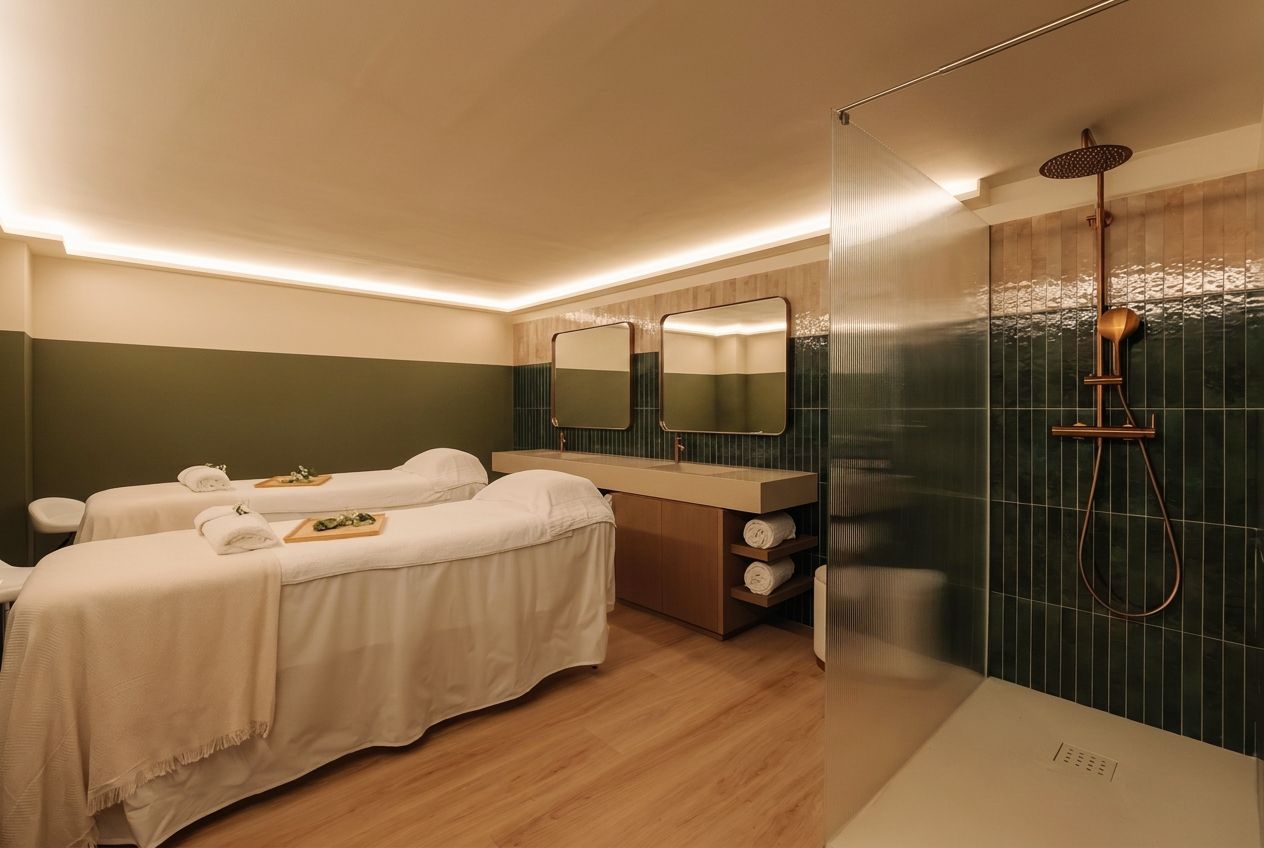 Sala de masajes con dos camillas de tratamiento, paredes verdes, suelo de madera y zona de ducha con paneles de cristal.