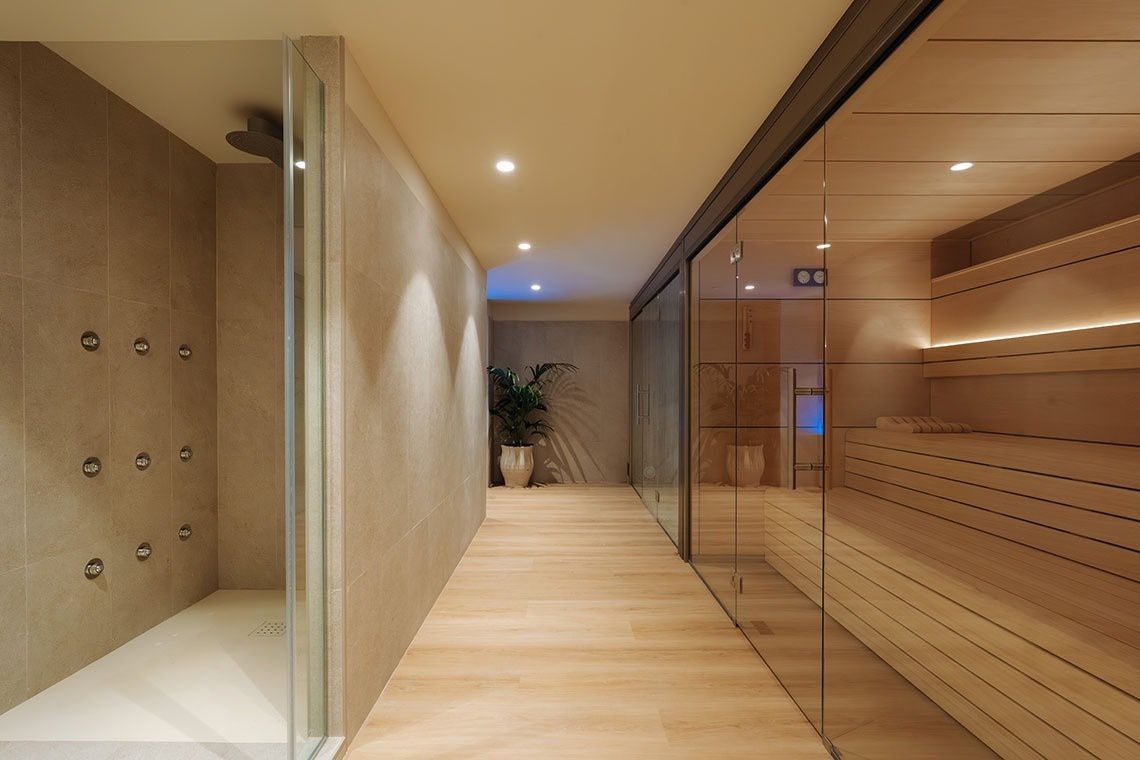 Pasillo de spa moderno con saunas de cristal, paneles de madera e iluminación empotrada cálida.