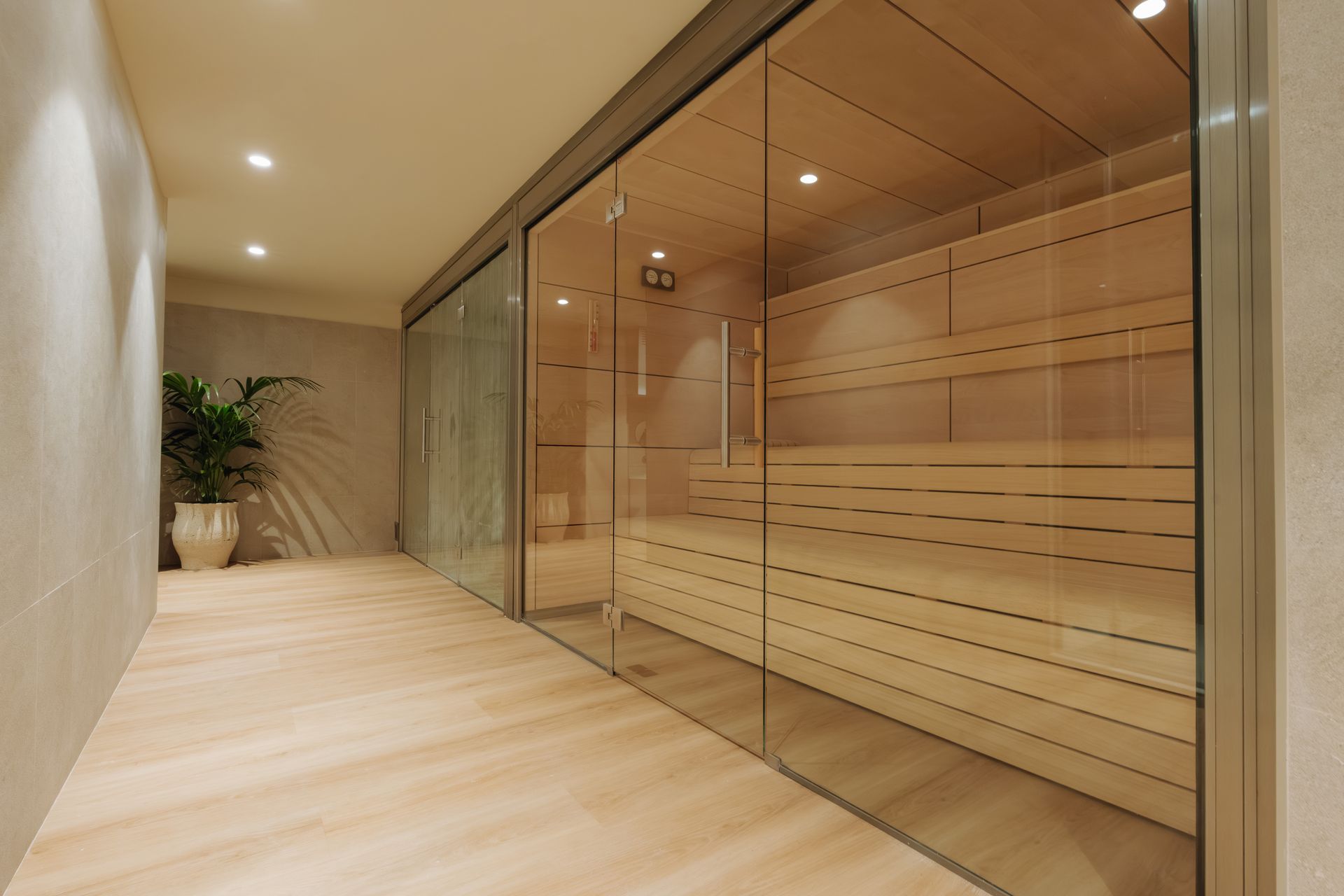 Pasillo moderno con sauna de paredes de cristal, suelos de madera clara y luces empotradas en el techo.