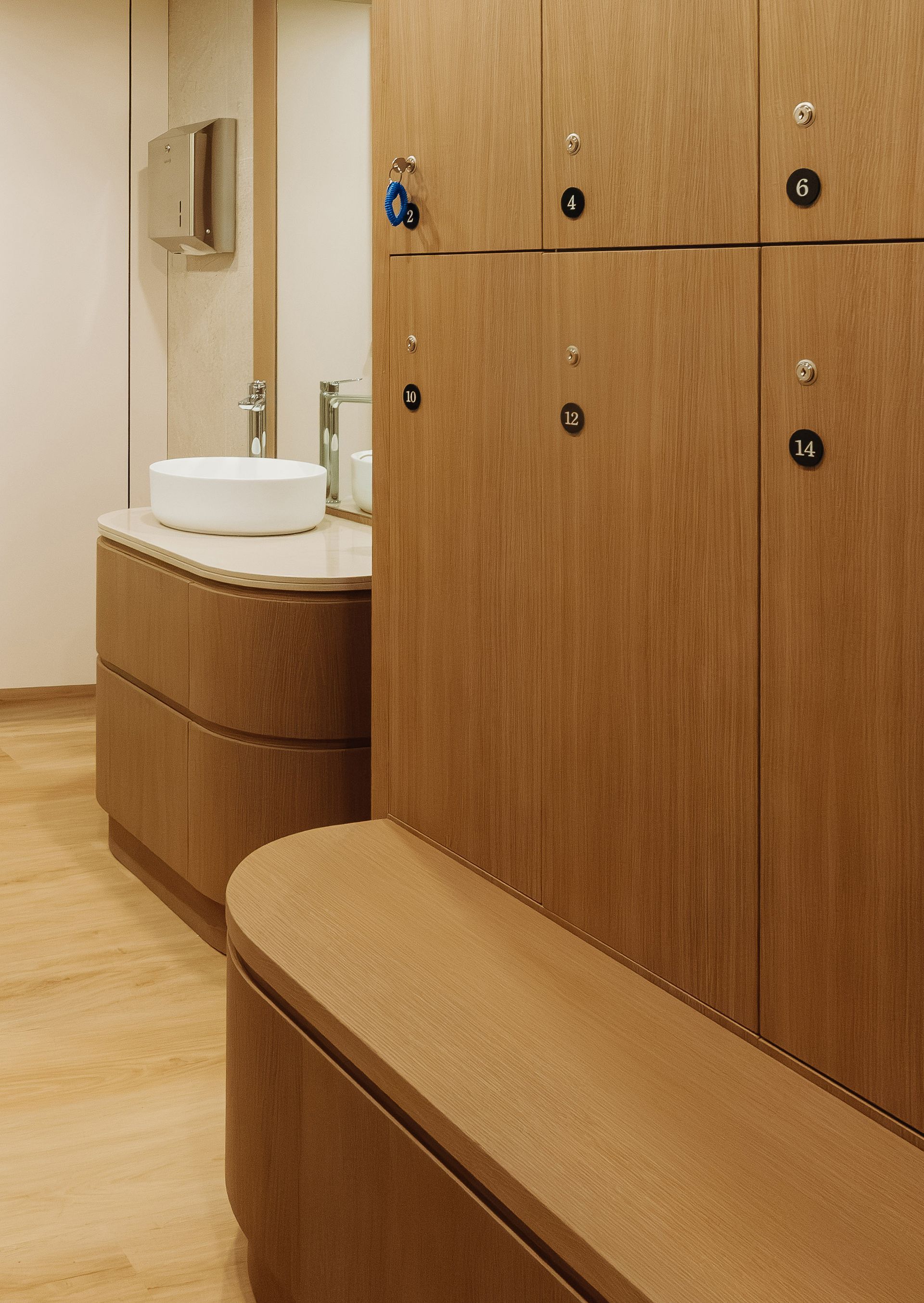 Interior de baño revestido de madera con banco curvo, lavabo y armarios a lo largo de la pared.