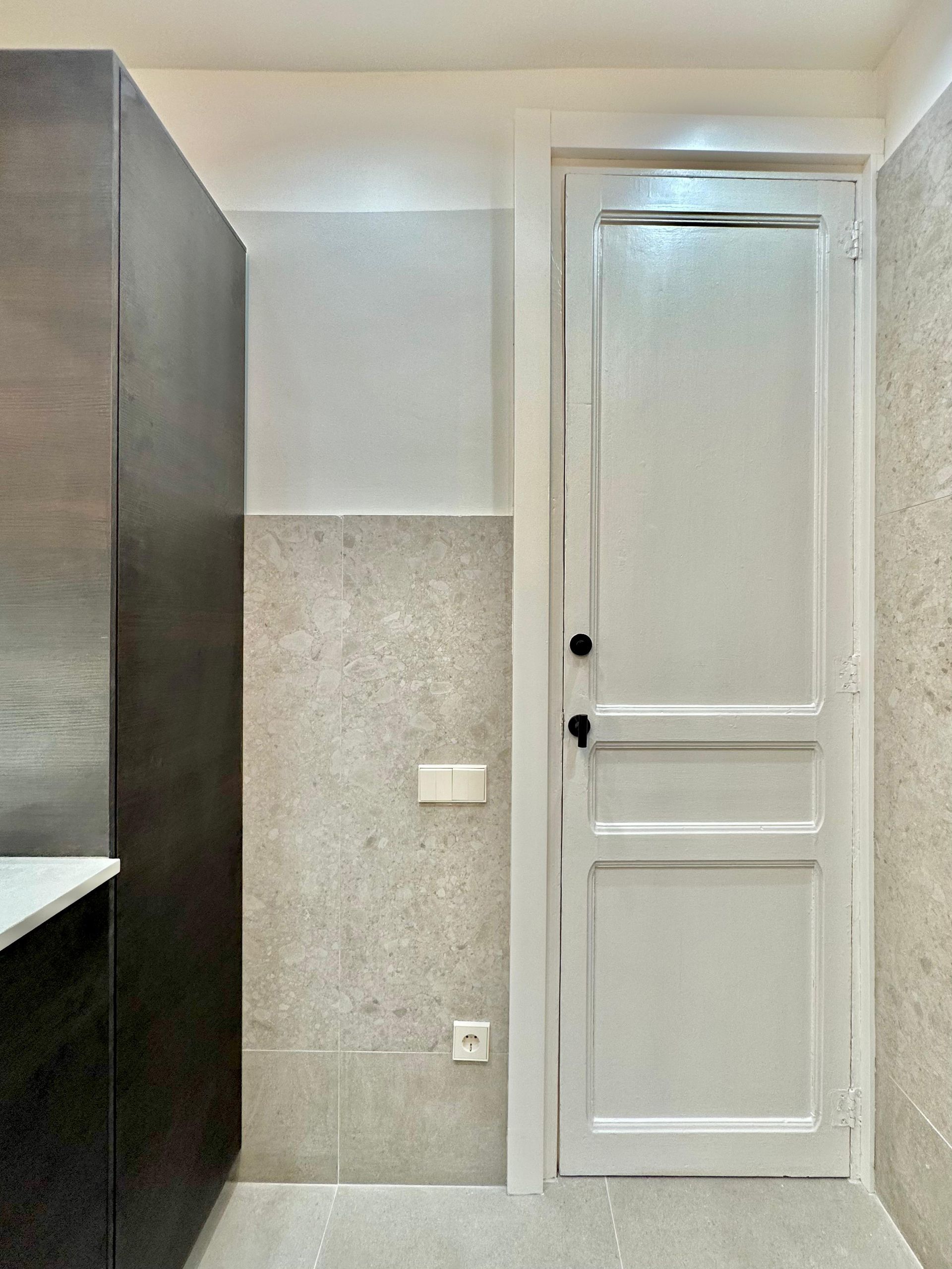 Pasillo estrecho con armario gris, pared alicatada y puerta blanca con paneles al final.