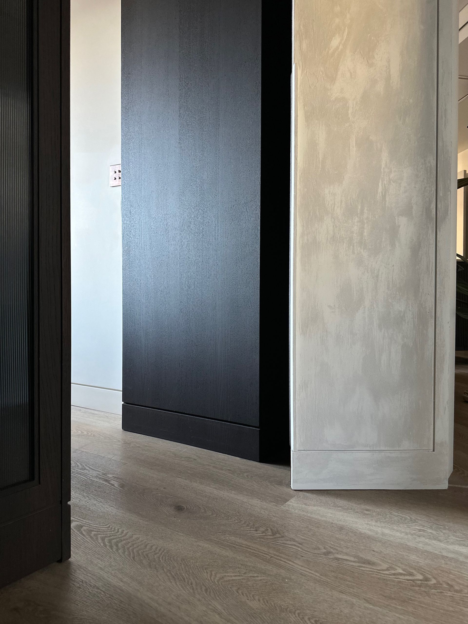 Interior moderno con suelo de madera, panel de pared negro y una puerta gris claro parcialmente abierta.