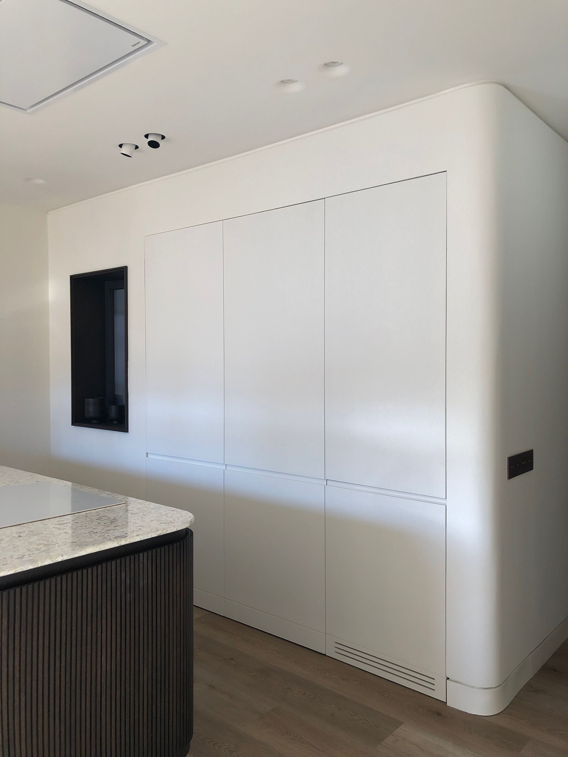 Cocina moderna con armarios empotrados blancos, ventana negra y encimera moteada.