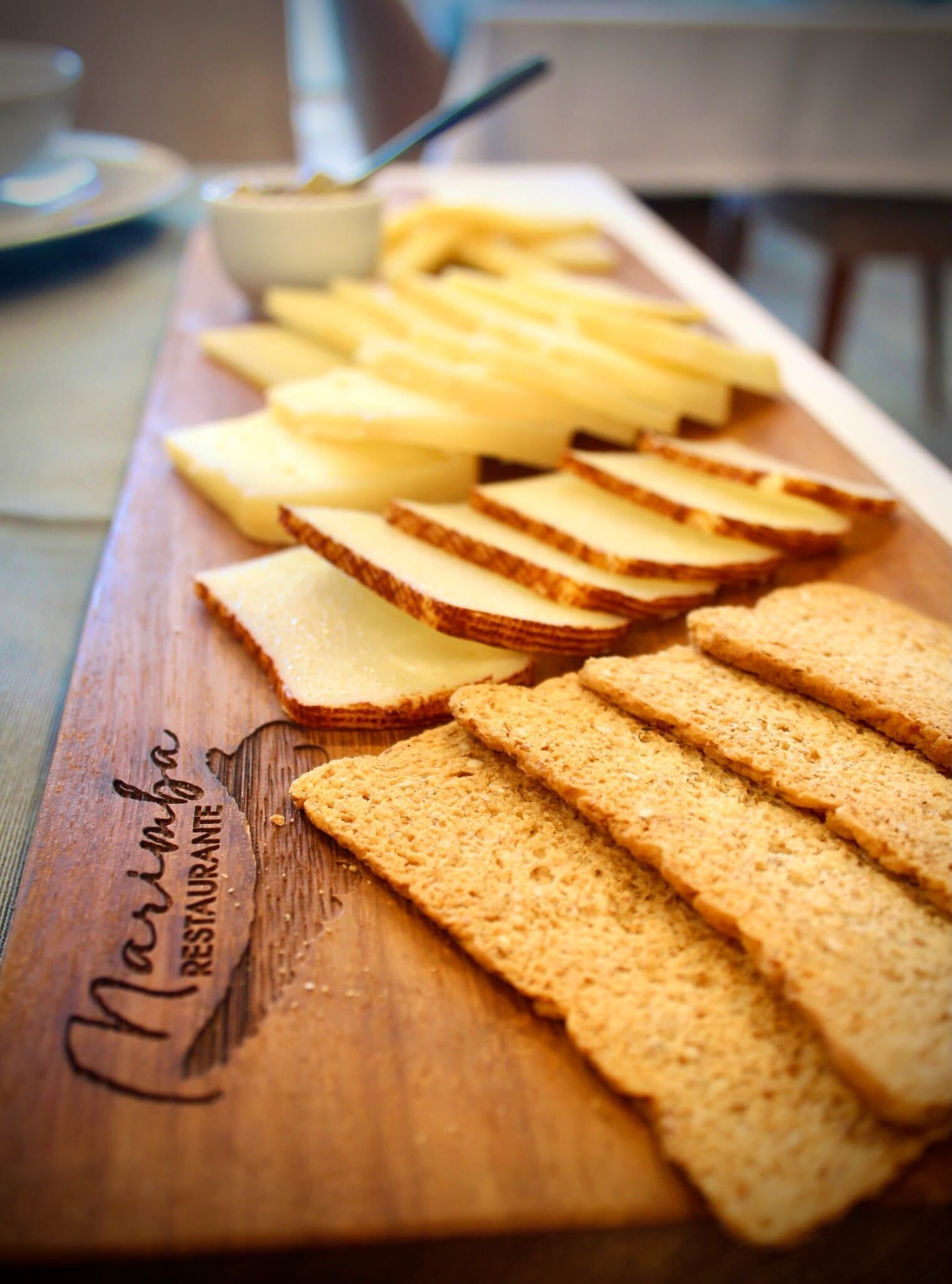 Uma tábua de corte de madeira coberta com fatias de queijo e biscoitos.