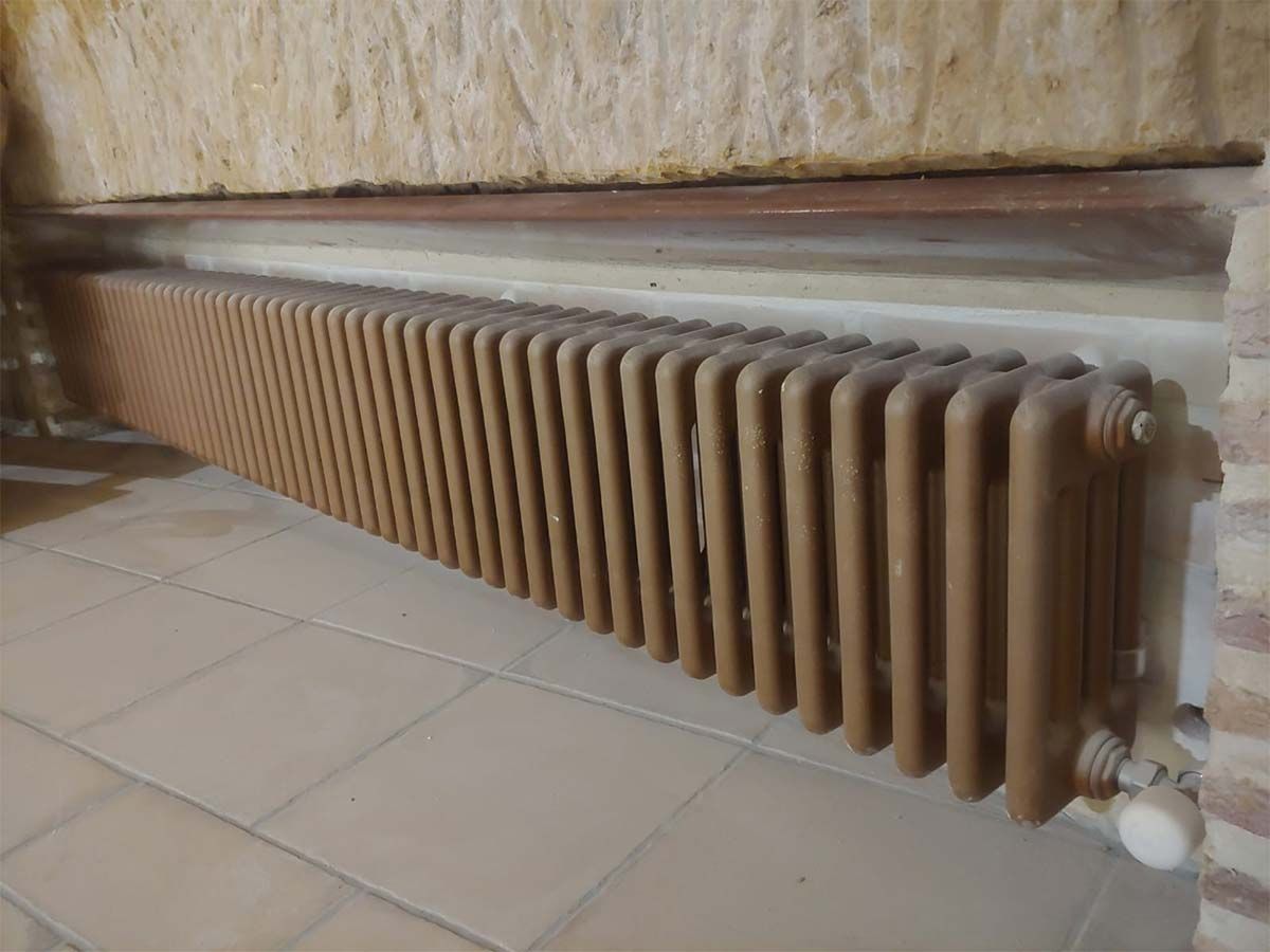 Un radiador marrón está sobre un suelo de baldosas al lado de una pared de ladrillos.