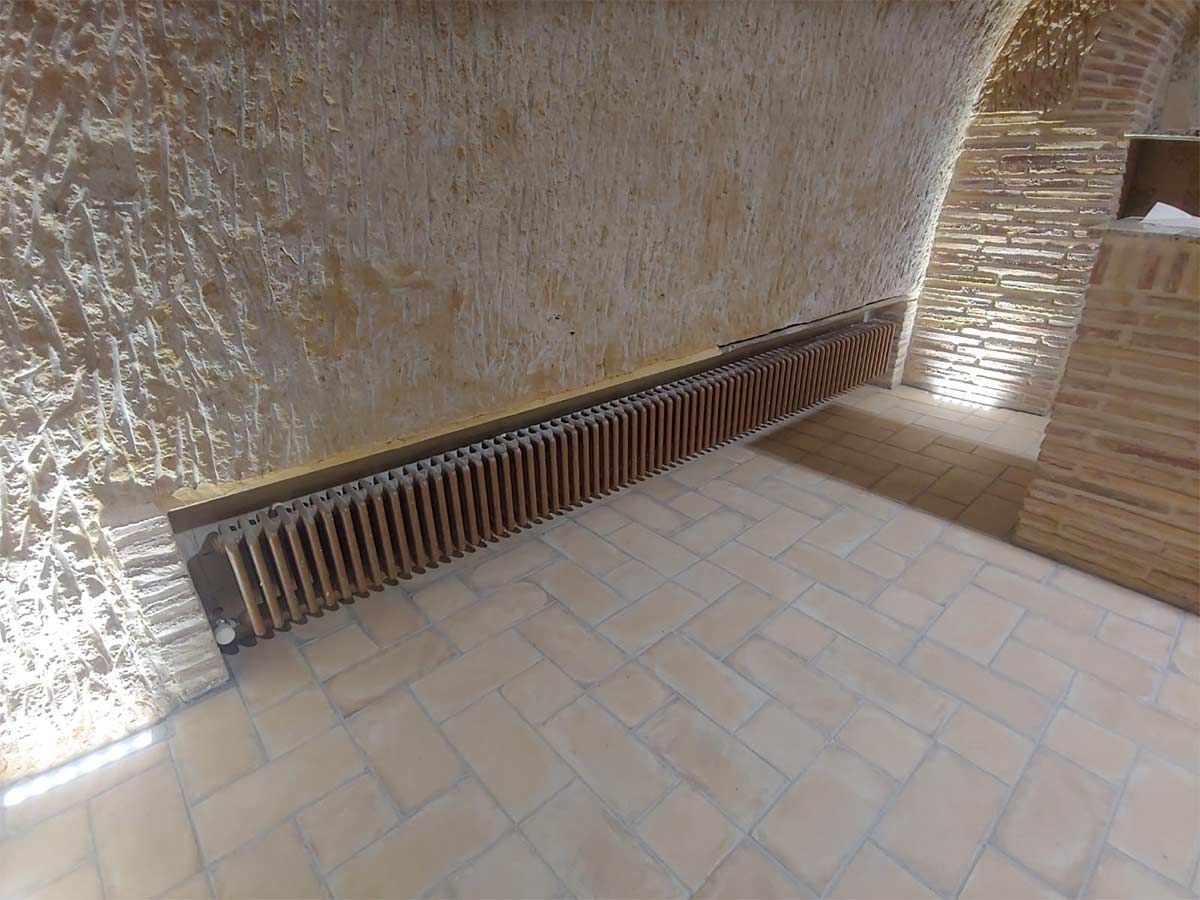 Una habitación con una pared de ladrillo y un radiador de madera en el suelo.