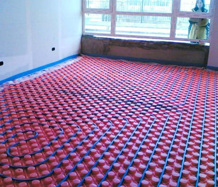 Una mujer está parada en una habitación con un sistema de calefacción por suelo radiante de color rojo y azul.