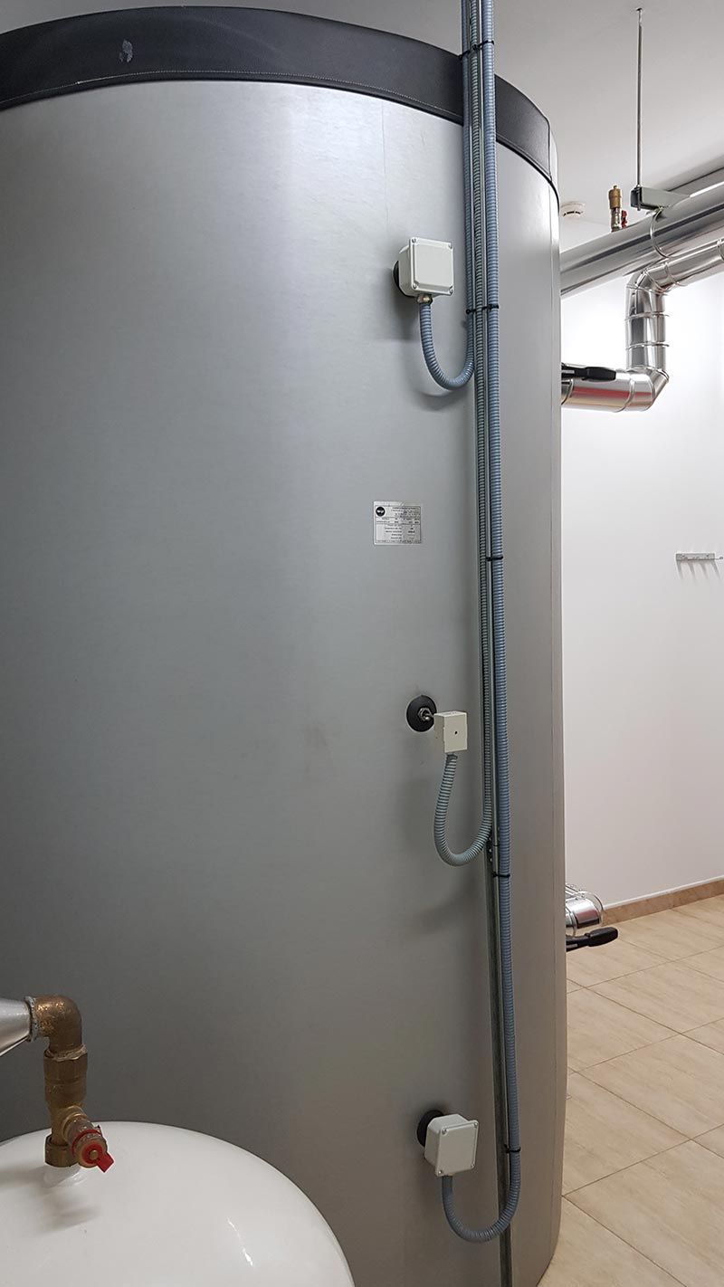 Un gran calentador de agua gris está ubicado al lado de un inodoro en una habitación.