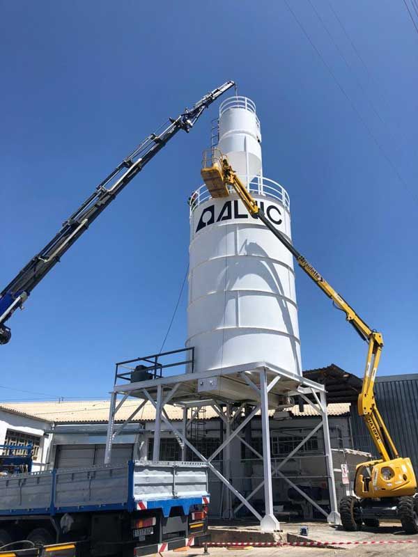 Una grúa está levantando un silo de hormigón delante de un edificio.