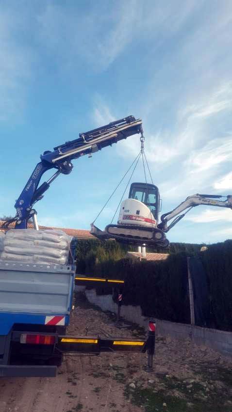 Una grúa está levantando una excavadora hacia un camión.