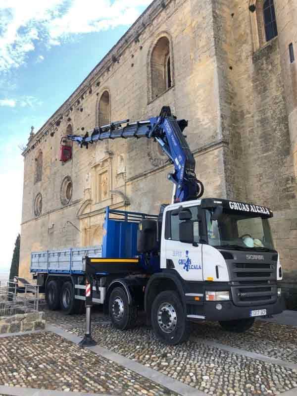 Un camión azul y blanco con una grúa en la parte trasera está estacionado frente a un edificio.