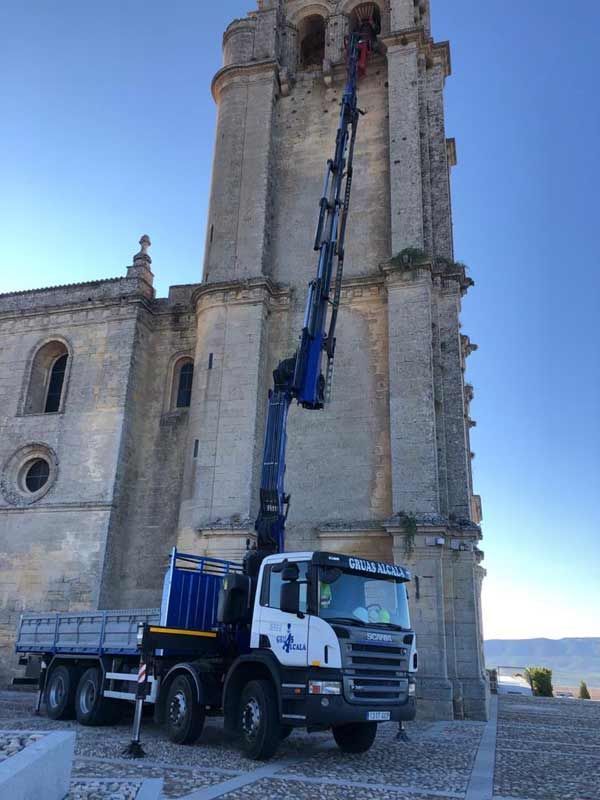 Un camión con una grúa acoplada está aparcado delante de un gran edificio.