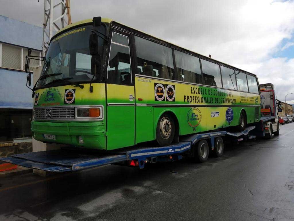 Un autobús verde y amarillo está siendo transportado en un remolque.