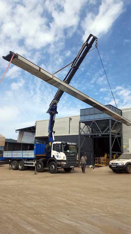 Una grúa está levantando una gran pieza de metal frente a un edificio.