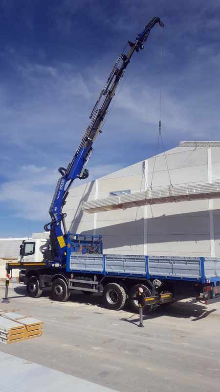 Un camión azul con una grúa en la parte trasera está estacionado frente a un edificio.