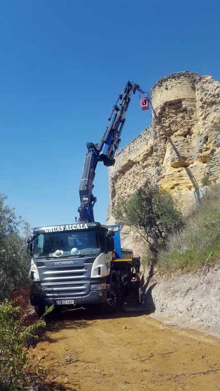 Un camión con una grúa acoplada circula por un camino de tierra.