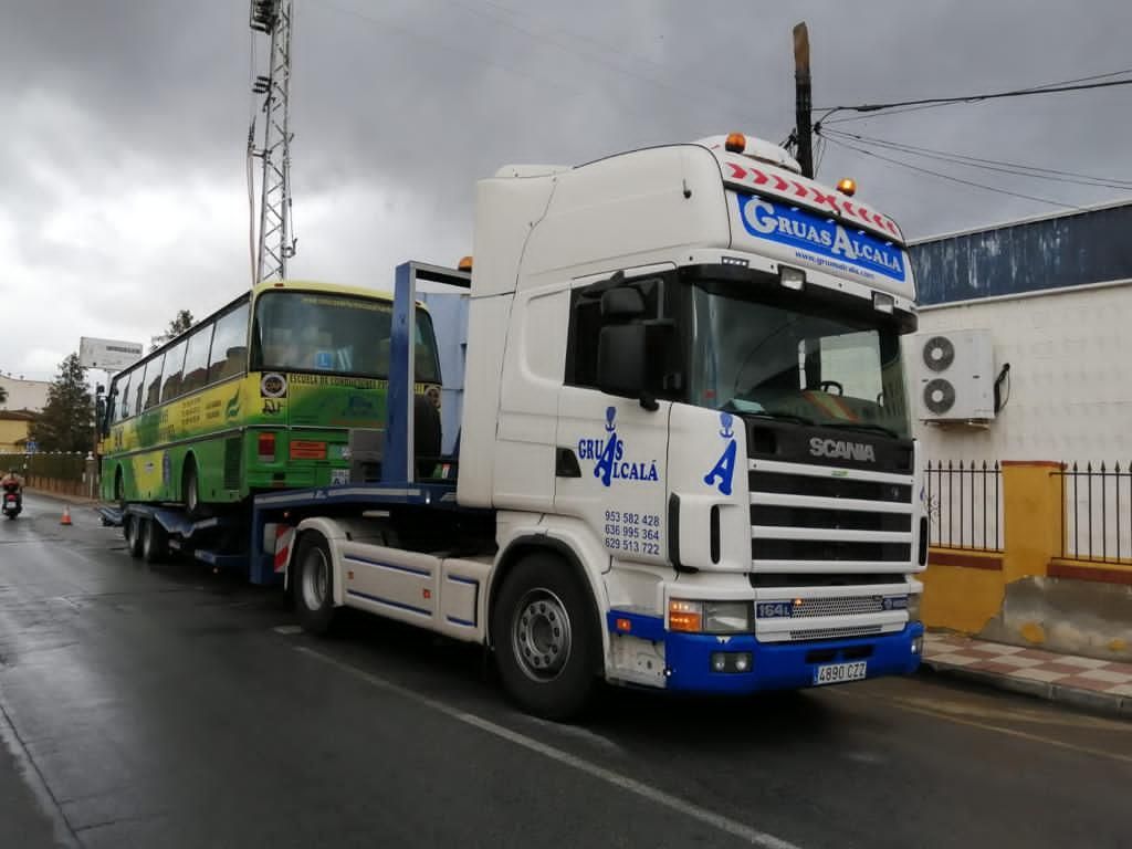 Un camión Scania transporta un autobús verde.