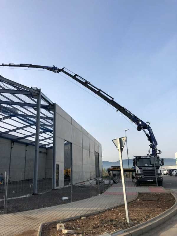 Un camión con una grúa acoplada está estacionado delante de un edificio en construcción.