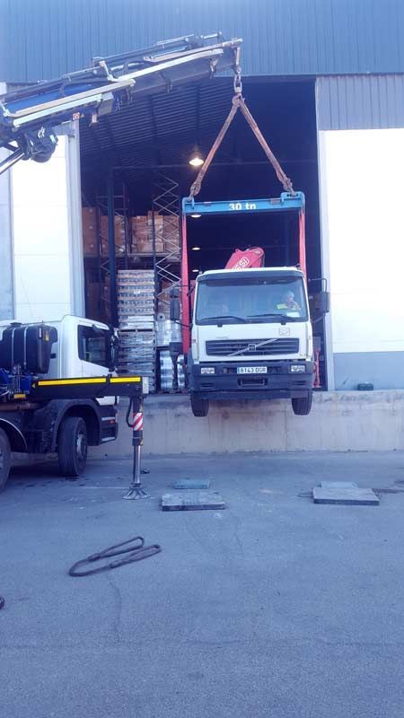 Un camión está siendo elevado hacia un almacén mediante una grúa.