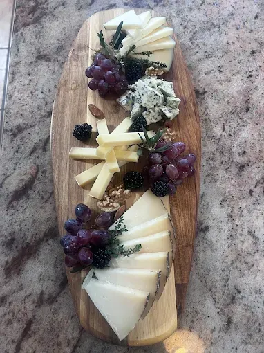 Una tabla de cortar de madera cubierta con queso en rodajas, uvas, moras y nueces.