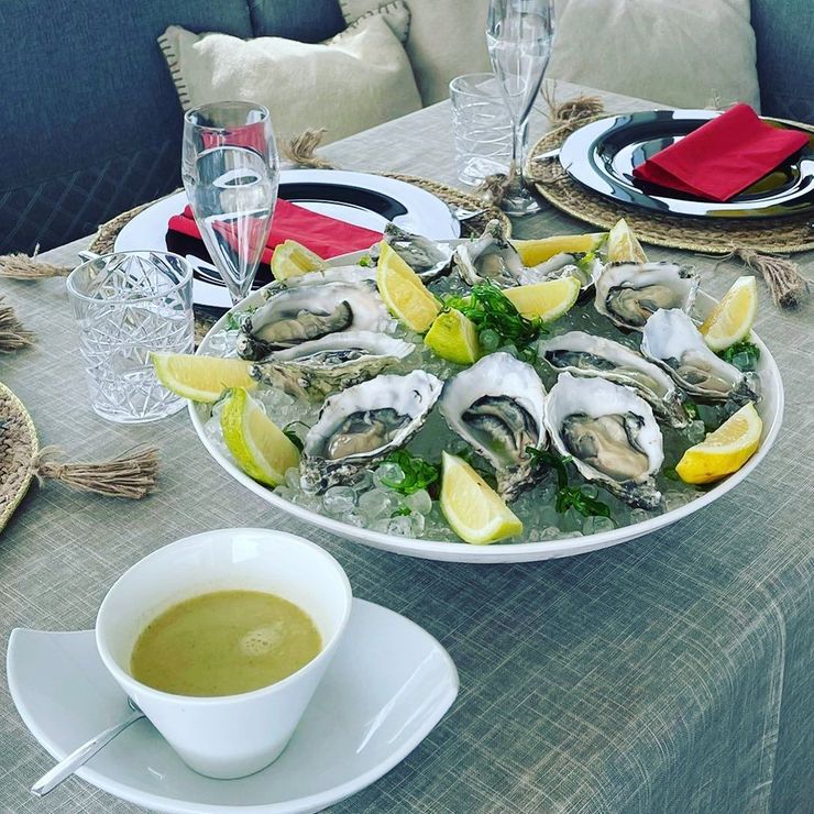 Un plato de ostras en hielo junto a una taza de sopa en una mesa.