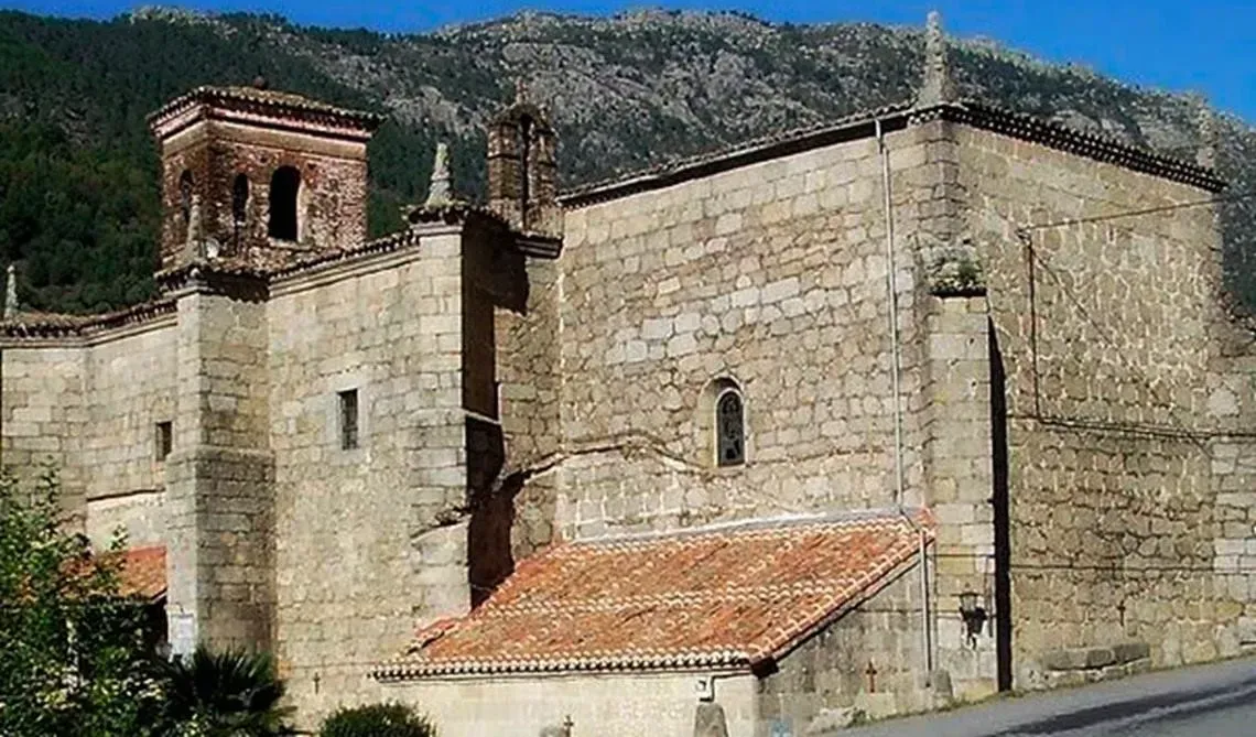 Un gran edificio de piedra con techo de tejas rojas está rodeado de montañas.