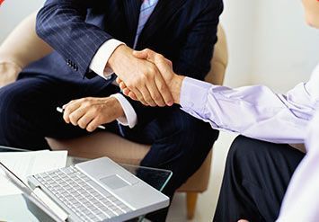 Dos empresarios dándose la mano junto a un ordenador portátil en una sala de reuniones.