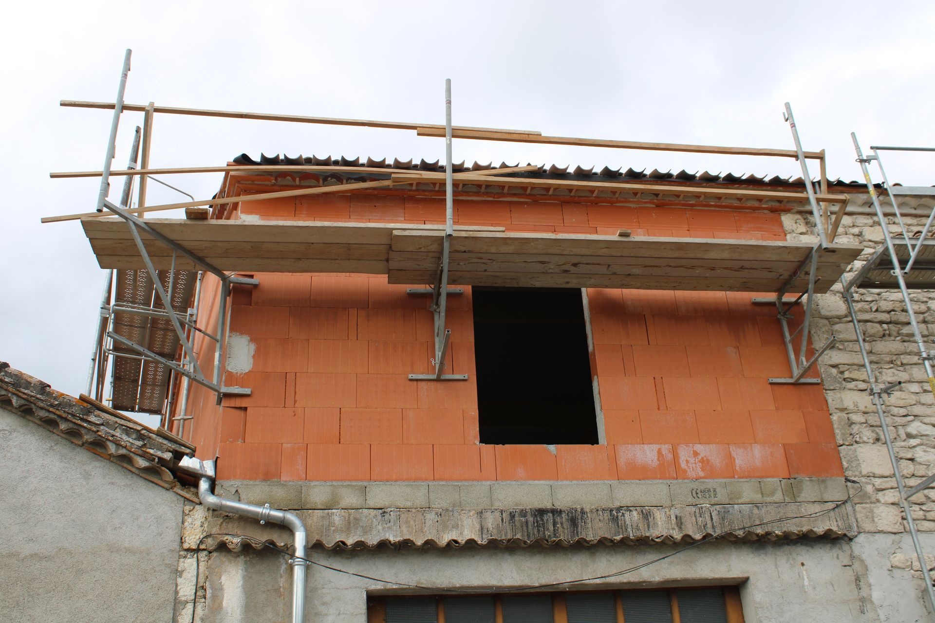 Maison en briques partiellement construite avec échafaudages et une fenêtre ouverte.