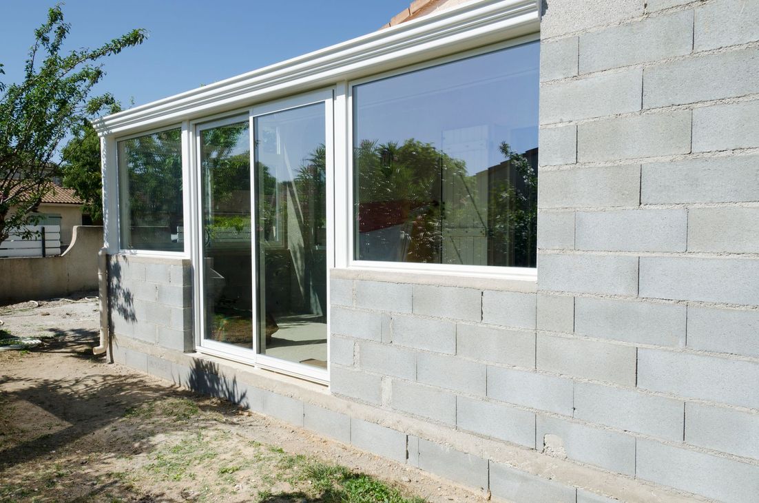 Façade d'une maison partiellement construite avec de grandes fenêtres et un mur en parpaings.